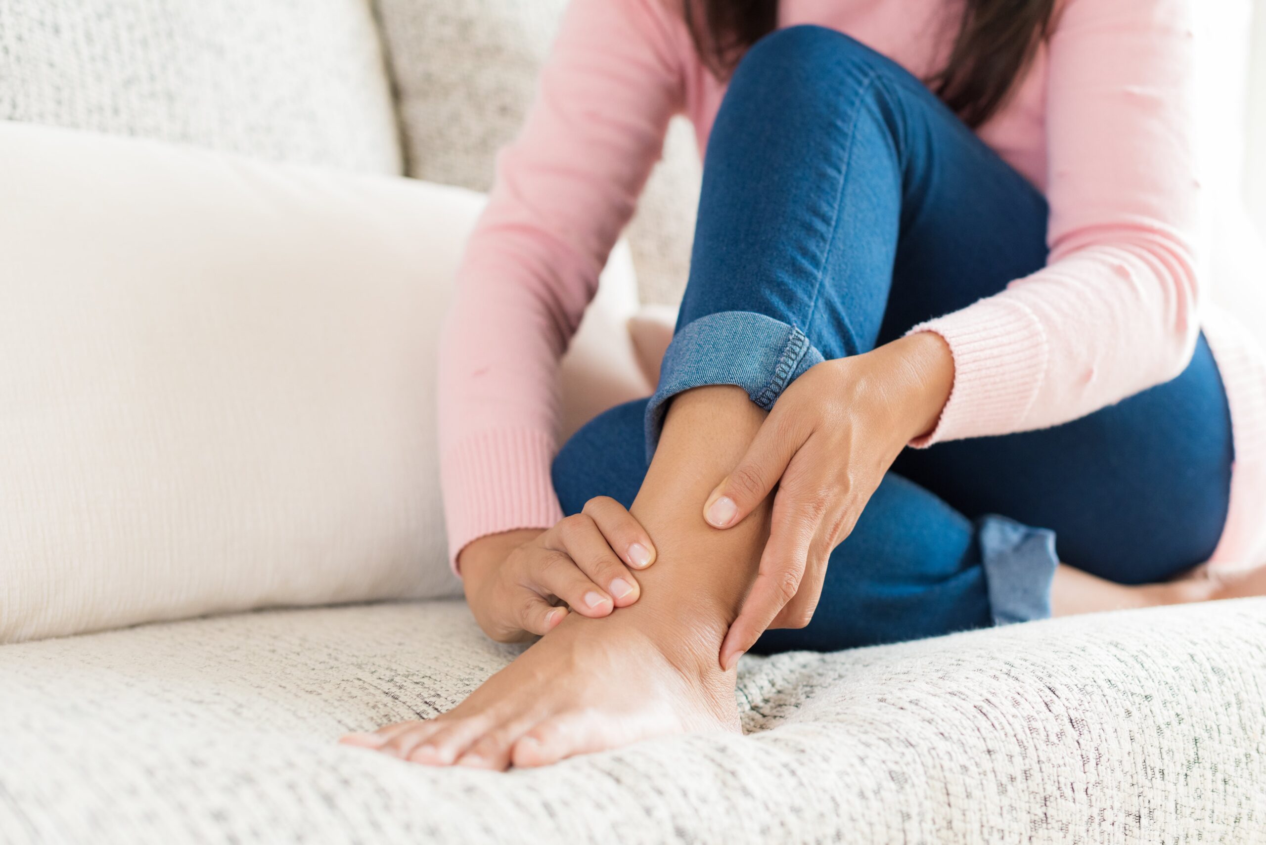 Woman holding ankle in pain on couch