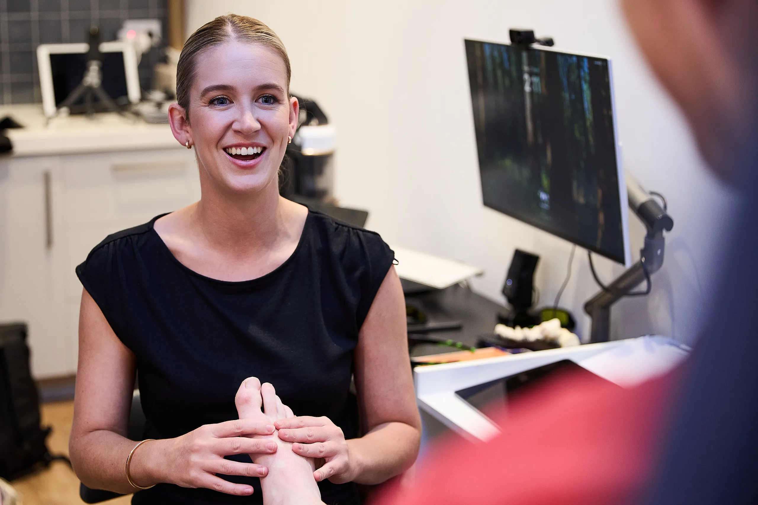 Pure Physio podiatrist Ella Wright conducts a consultation with a client at a desk in the Collins Street clinic treatment room, with a computer monitor visible.